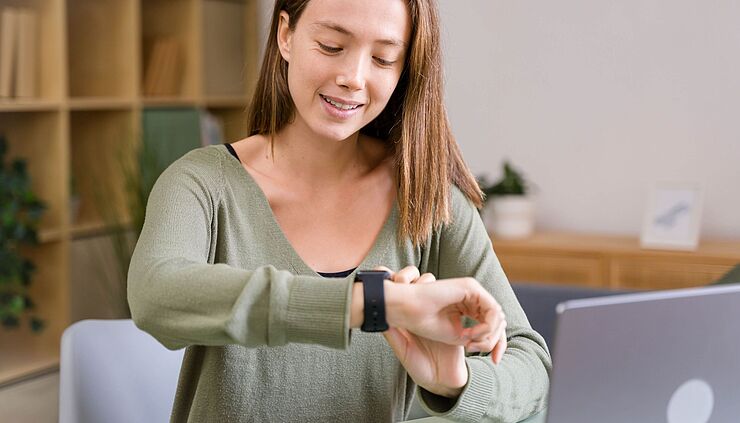 Frau (Therapeutin) schaut in ihrem Arbeitszimmer auf die Uhr