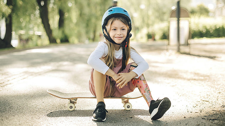 Mädchen mit Unterschenkelprothese sitzt auf einem Skateboard