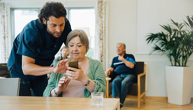 Pfleger erklärt Seniorin etwas am Smartphone